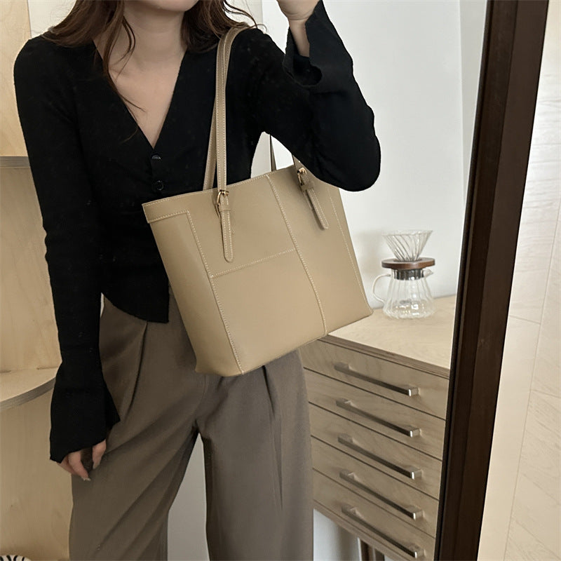 Large shoulder bag in beige carried by woman wearing black top and brown pants indoors