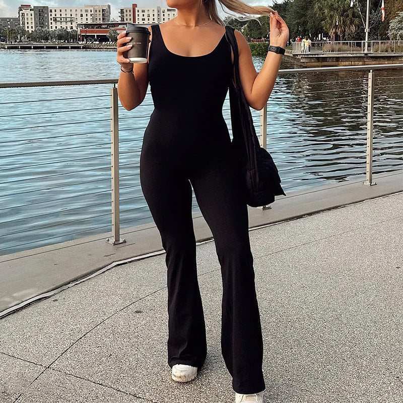 Woman wearing black slim fit jumpsuit for women holding coffee cup near waterfront with buildings in background
