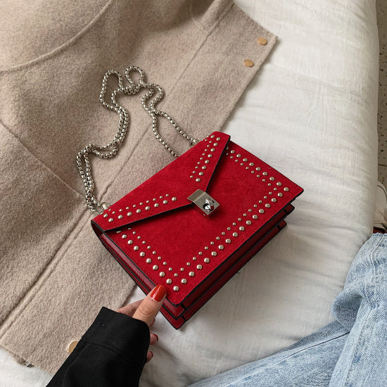 Women's red leather purse with chain featuring silver studs and a lock clasp on a beige and white background